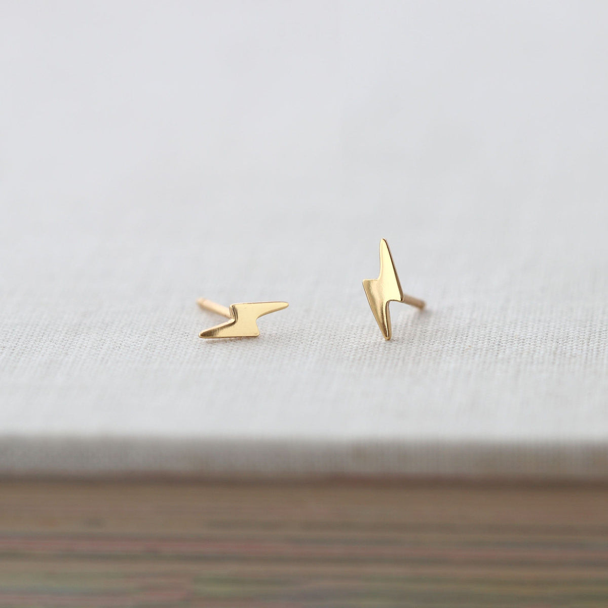 Gold Lightning Bolt Stud Earrings on a gray book