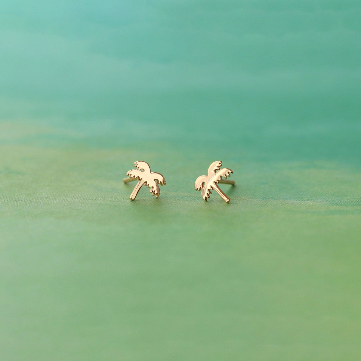 Gold Palm Tree Stud Earrings on a sea green background