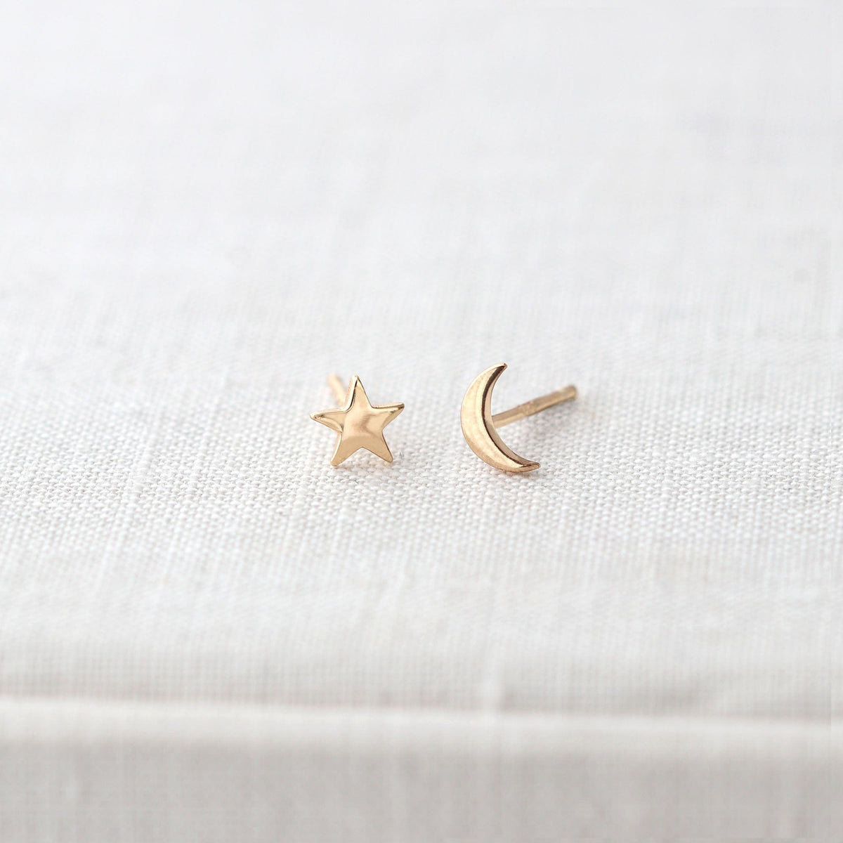 Gold Star and Moon Stud Earrings on a white linen book