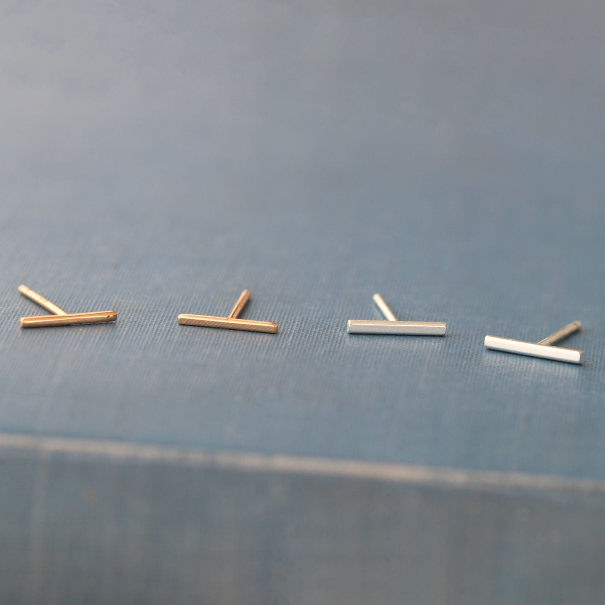 Bar Dash Stud Earrings in 18K gold vermeil and sterling silver on a slate blue book