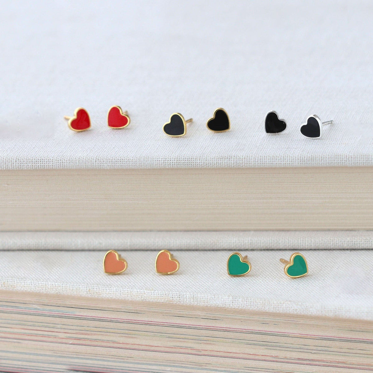 Petite Heart Enamel Stud Earrings in red, black, peach and green on a stack of books