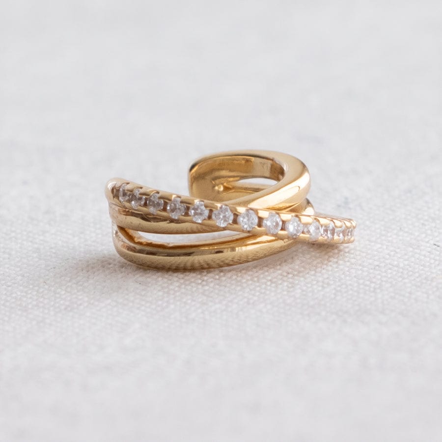 A gold wrap ring with a row of clear pavé-set round stones, photographed on a textured light gray fabric background.