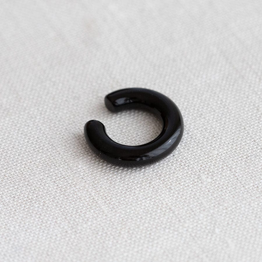 A glossy black open-ended C-shaped ring, likely made of black onyx resting on a textured off-white fabric background.