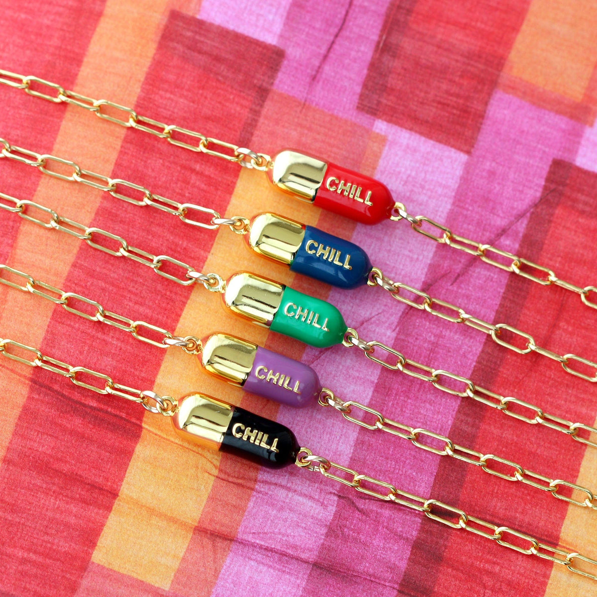 Chill Pill Bracelets in a row of enamel colors on pink and orange plaid fabric