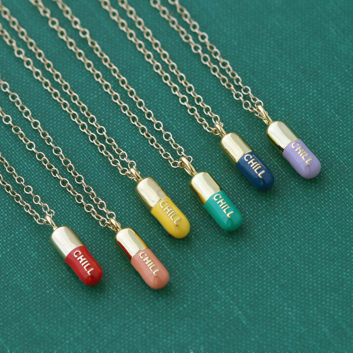 Chill Pill necklaces in a row of enamel colors, from coral red and sunshine yellow to emerald, navy and periwinkle