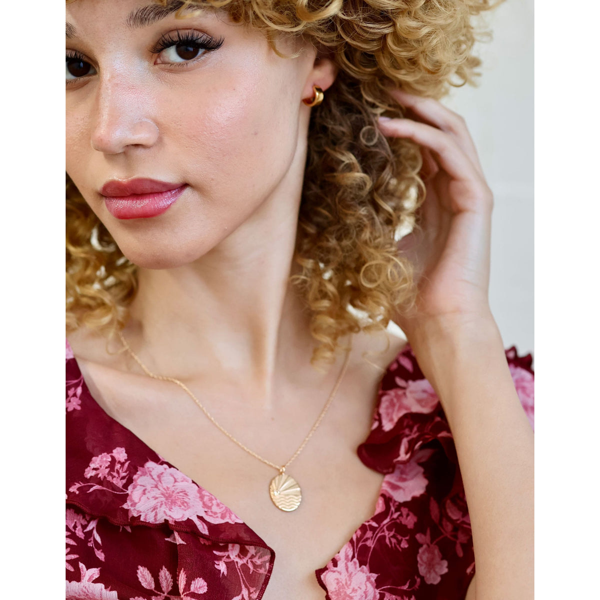 Woman with curly hair in a floral top wearing the gold Ray of Sunshine Charm Necklace