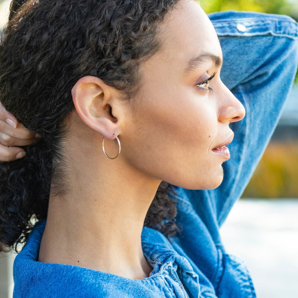 Woman with curly dark hair in a denim jacket wearing gold Featherweight Hoop Earrings