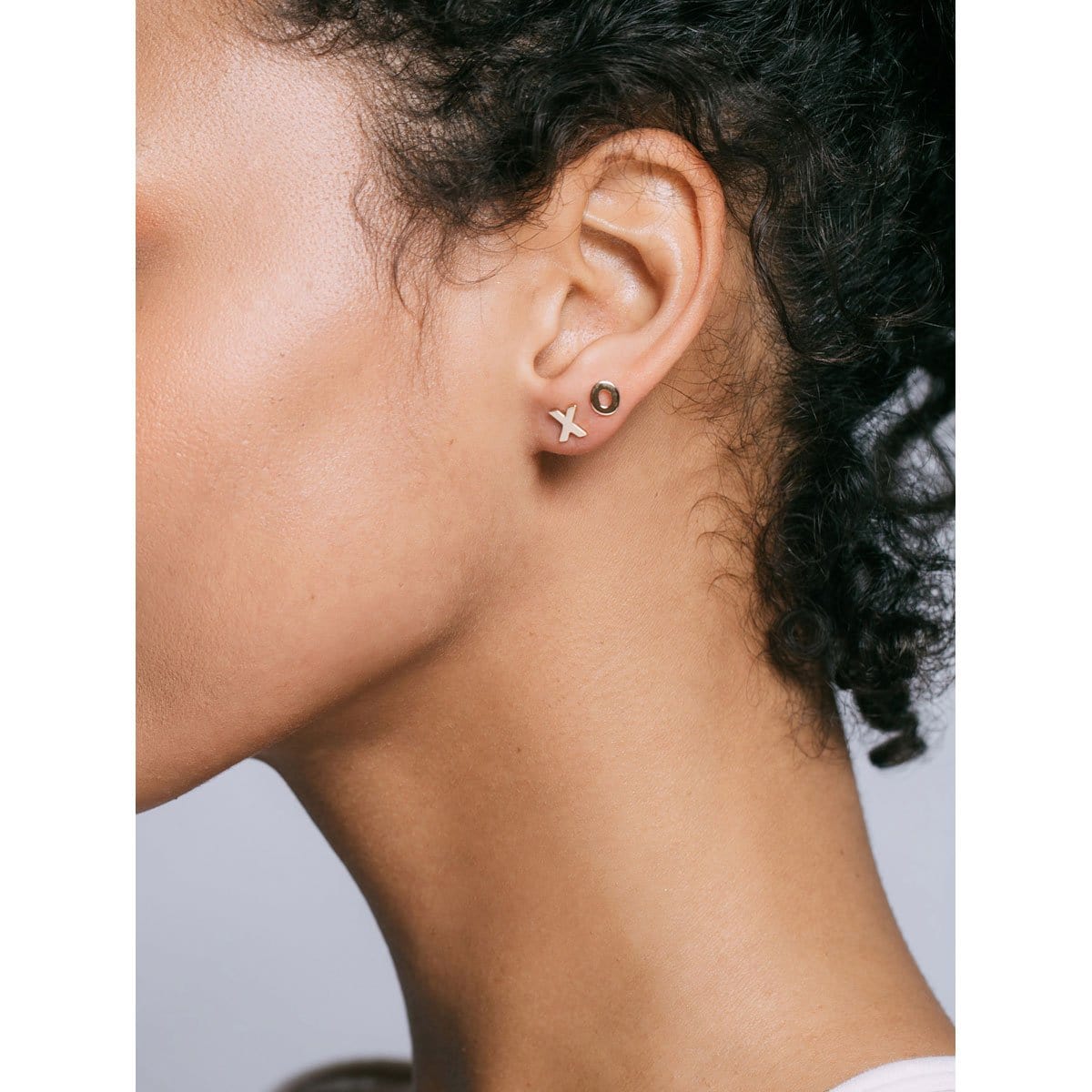 Profile of a woman with short curly dark hair wearing gold XO Stud Earrings