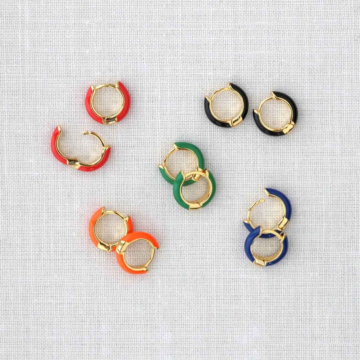 Enamel Huggie Hoop Earrings in assorted colors scattered on gray linen