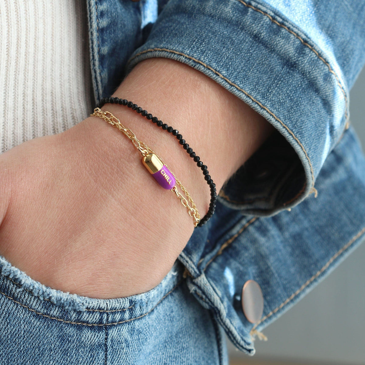 Wrist by a jeans pocket wearing an aubergine Chill Pill Bracelet with a black cord bracelet