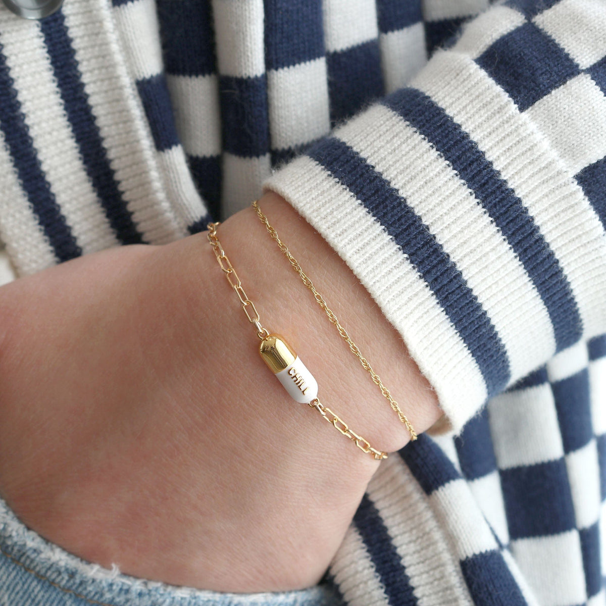 Wrist in a striped sleeve wearing a white Chill Pill Bracelet layered with a gold chain bracelet