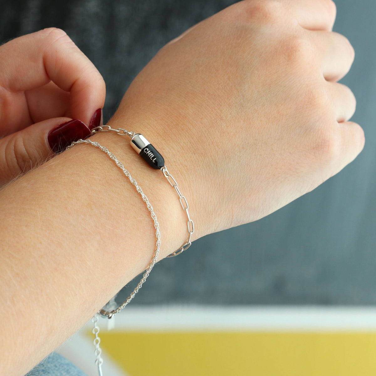 Wrist wearing a black Chill Pill Bracelet in sterling silver, layered with other bracelets