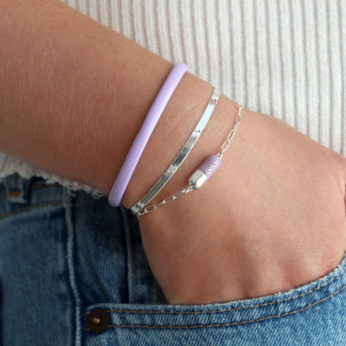 Wrist wearing a periwinkle Chill Pill Bracelet in sterling silver with a lavender bangle