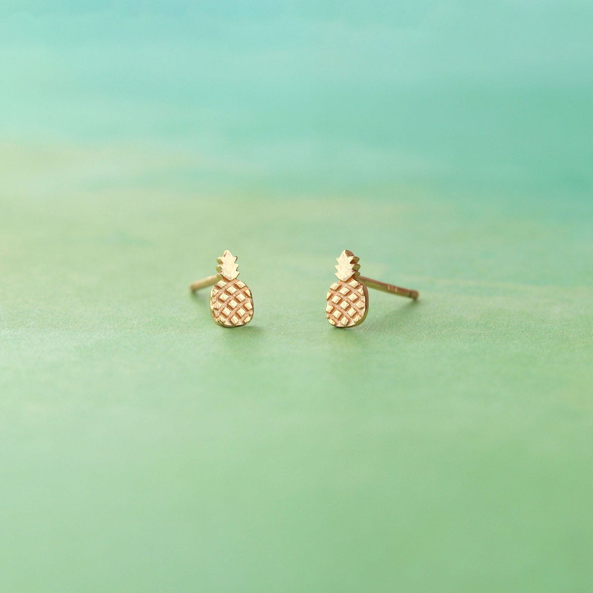 Gold Pineapple Stud Earrings on a sea green background