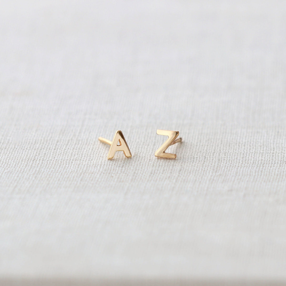 Gold A and Z Single Letter Stud Earrings on white linen