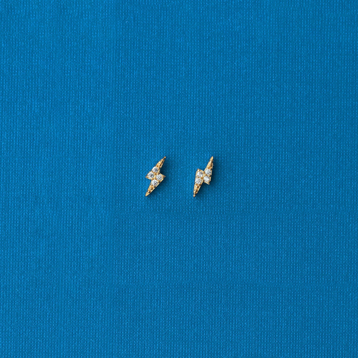 Gold Lightning Bolt Crystal Stud Earrings on blue fabric