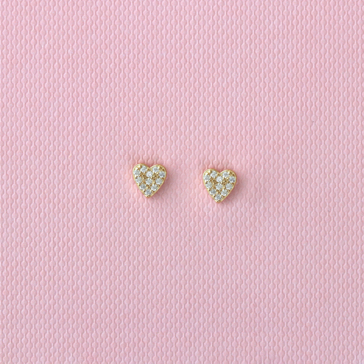 Gold heart crystal stud earrings on a pink background