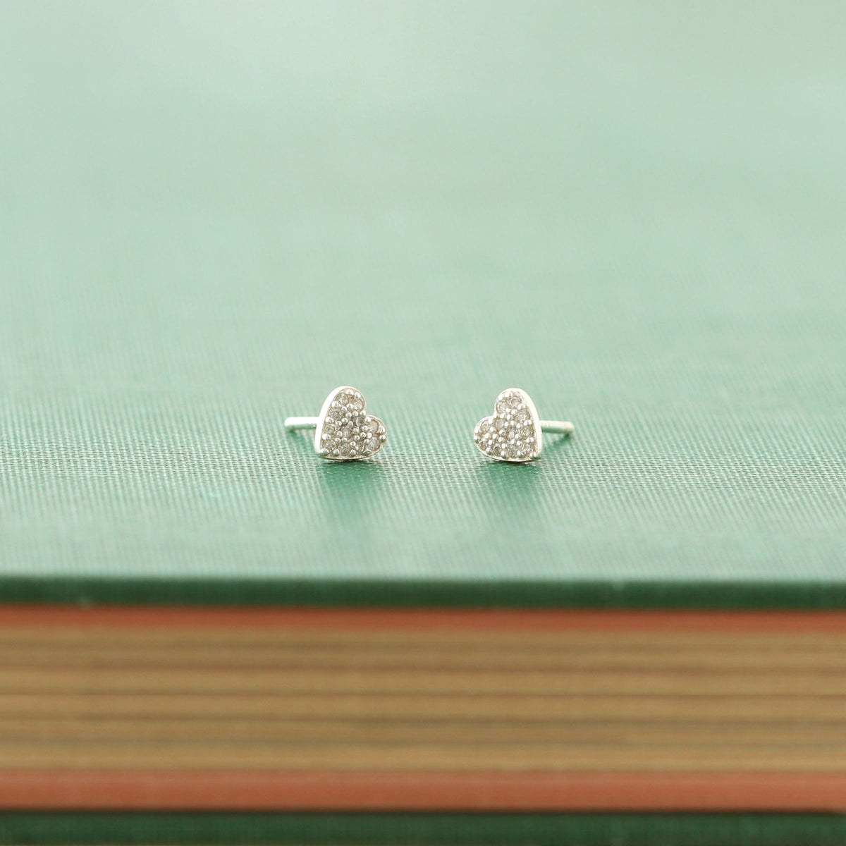Sterling silver heart crystal stud earrings resting on a green book