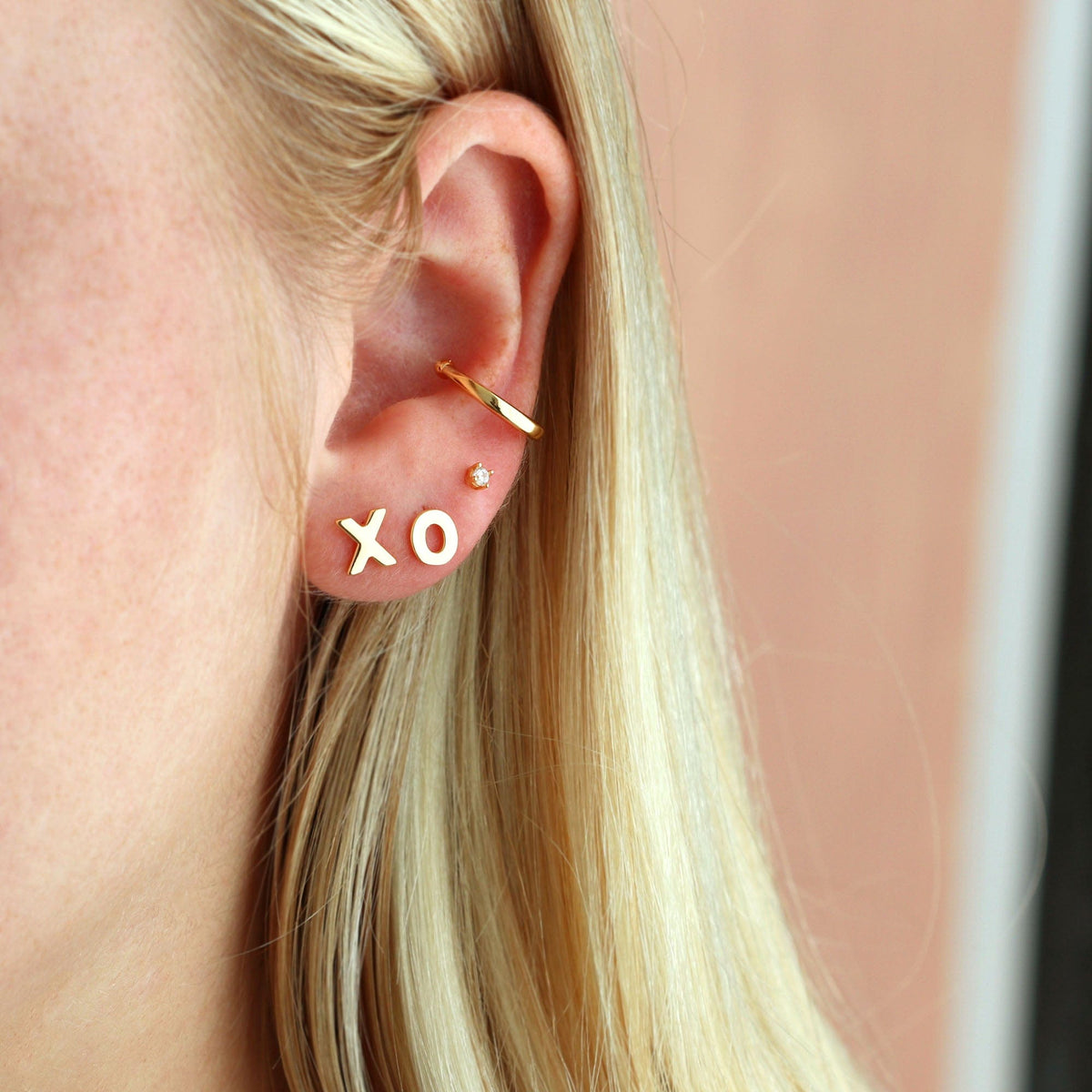 Gold X and O studs worn in an ear stack with long blonde hair