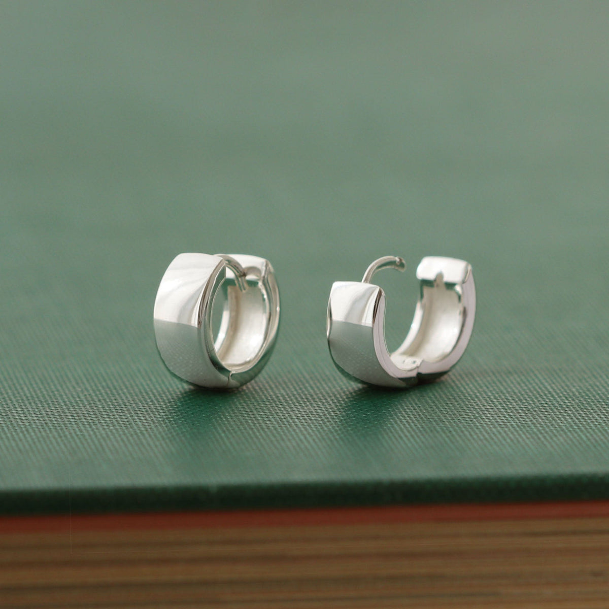 Wide Hinged Huggie Hoop Earrings in sterling silver on a green book