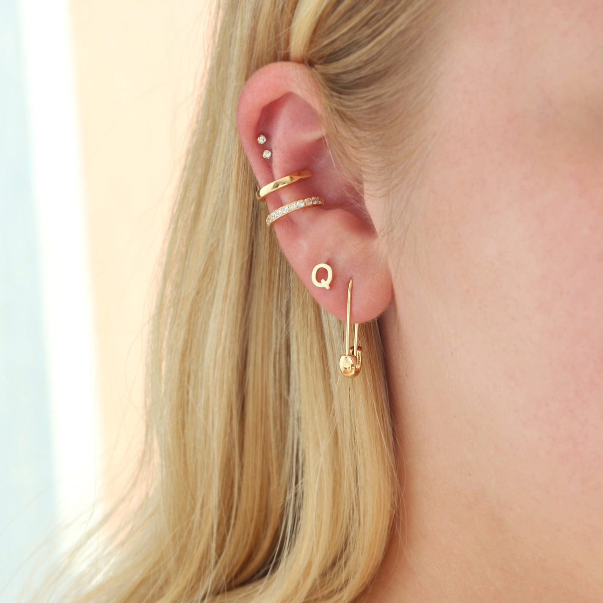 Gold Single Letter Stud worn in an ear stack with an ear cuff and a charm drop