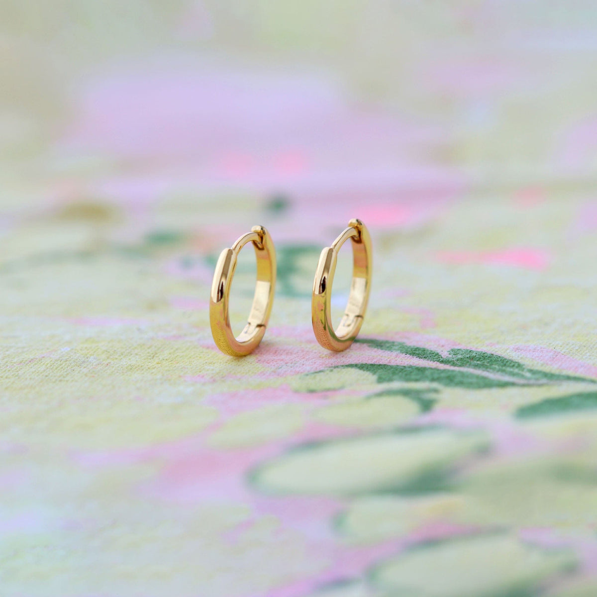 Classic 12mm Hinged Huggie Hoop Earrings in 18K gold vermeil on a pastel painted background