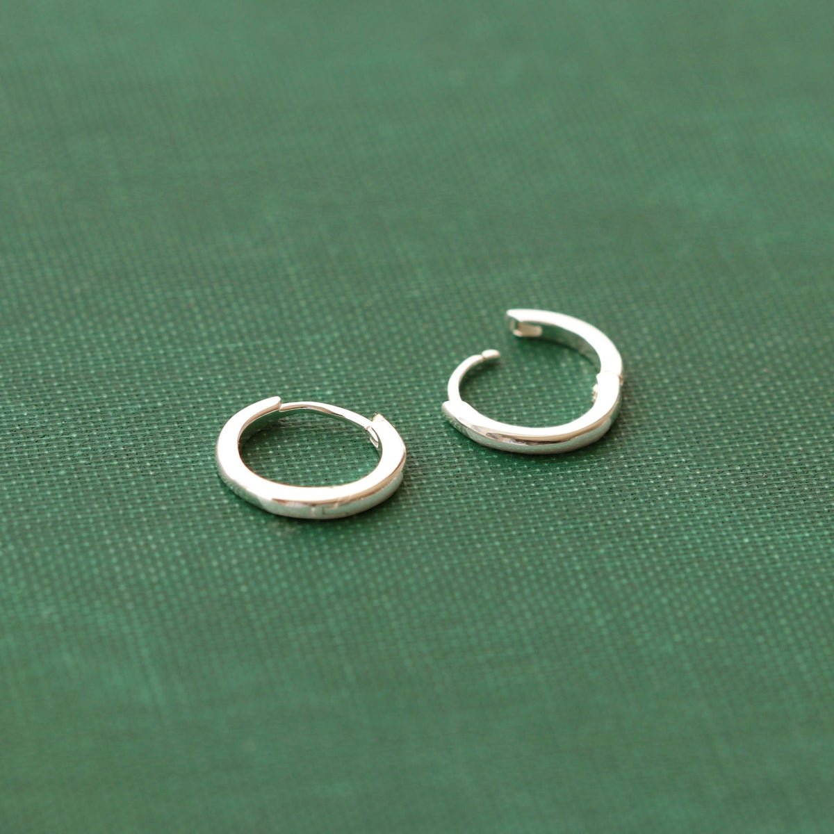 Classic 12mm Hinged Huggie Hoop Earrings in sterling silver on green fabric