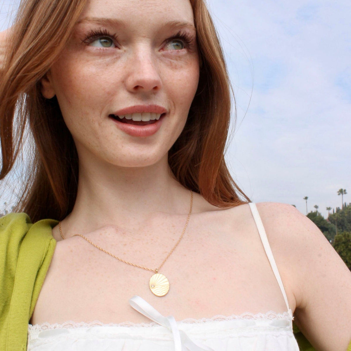 Smiling woman with long red hair wearing the gold Ray of Sunshine Charm Necklace