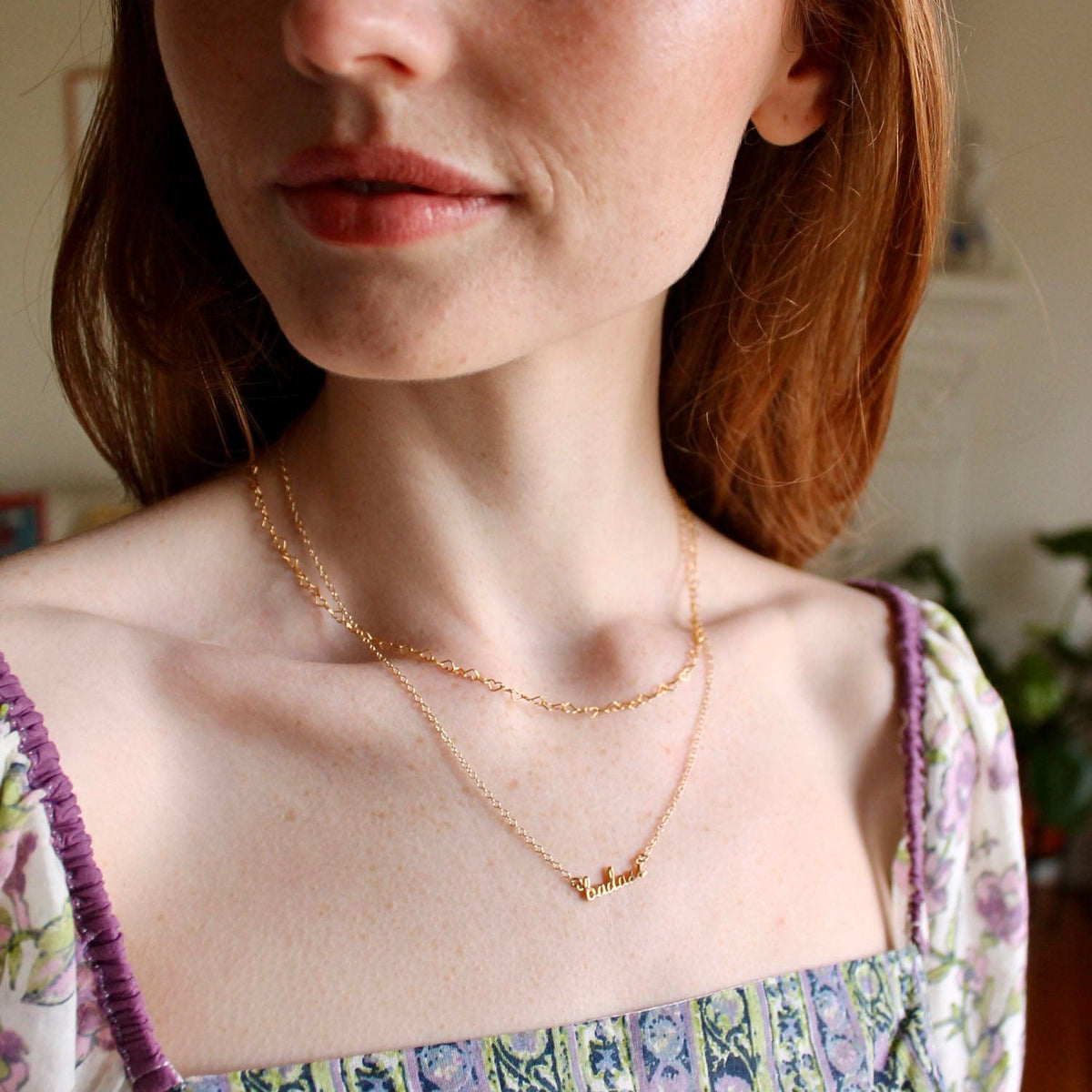 Woman with auburn hair in a floral top wearing the gold Badass Charm Necklace