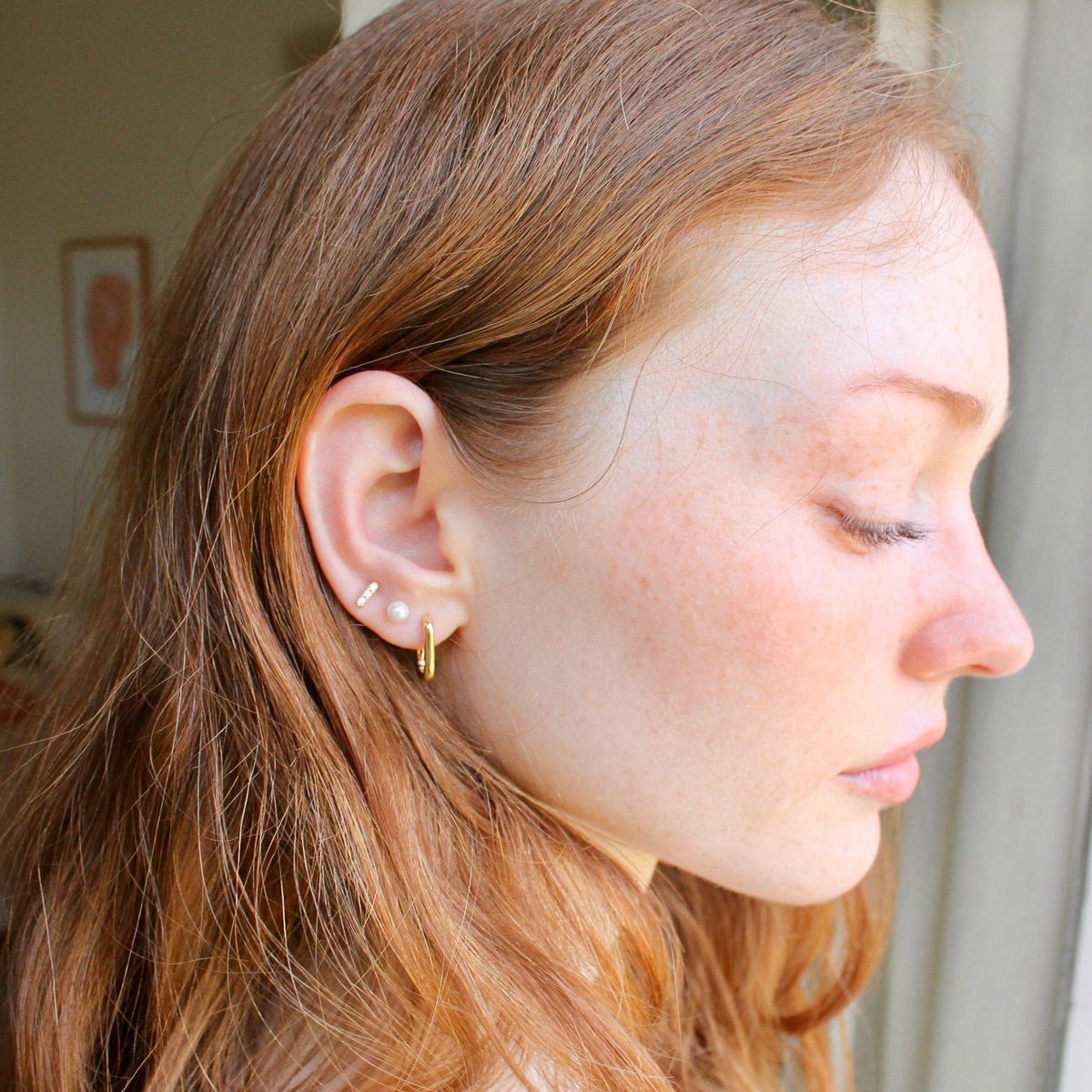 Woman with red hair wearing a gold Bar Dash Crystal Stud with a huggie hoop