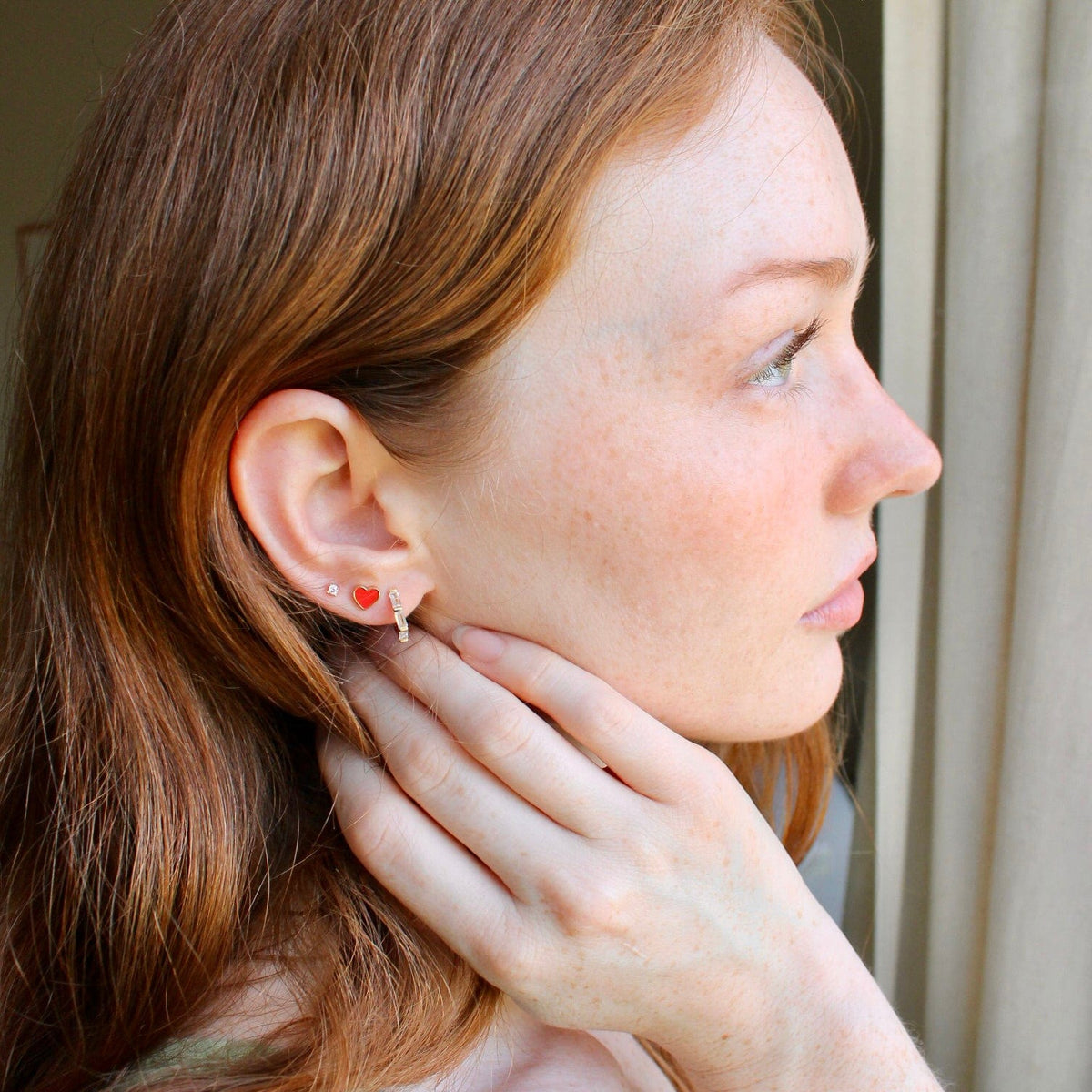 Woman with red hair, hand at her neck, wearing a Petite Heart Enamel Stud