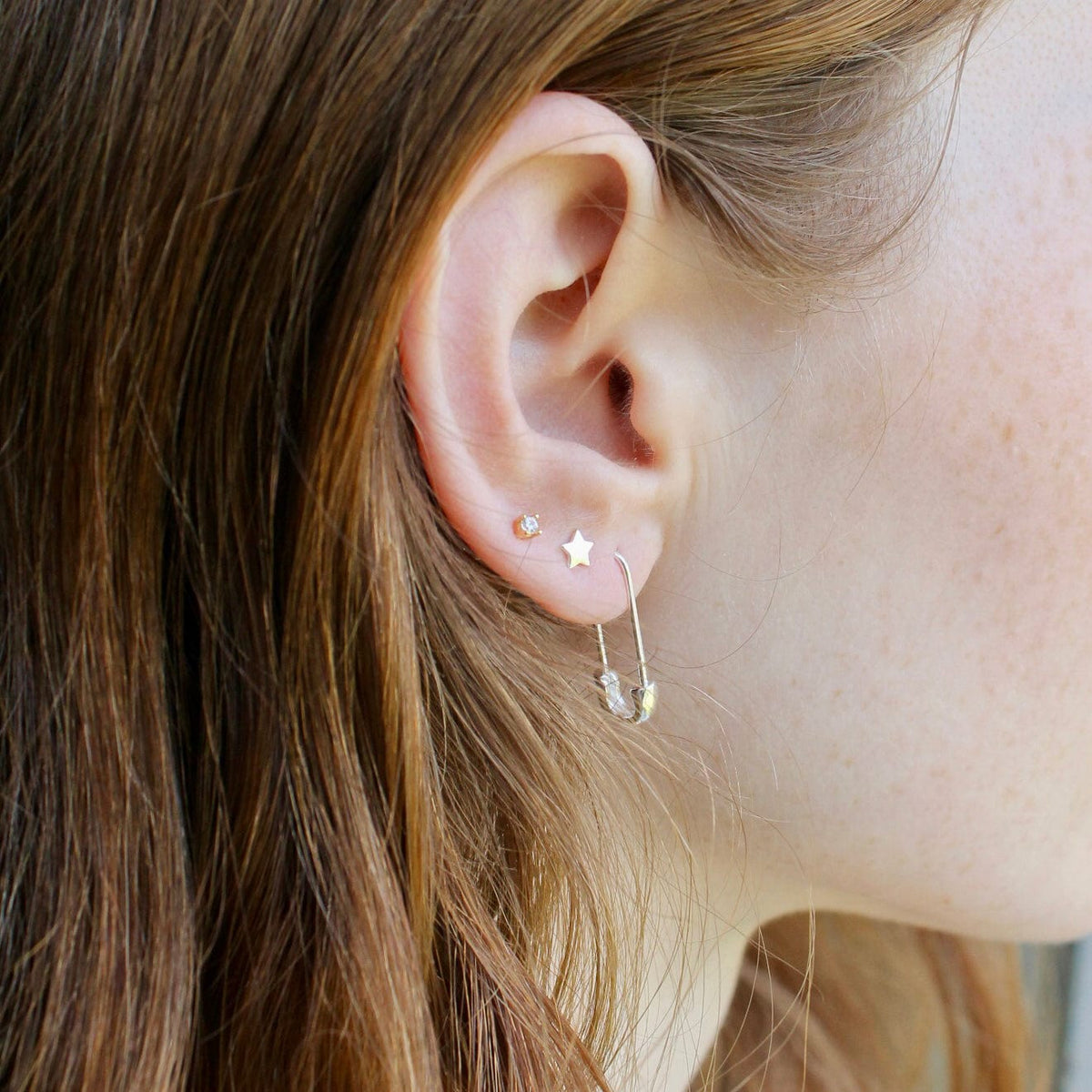 Woman with long brown hair wearing a Star Stud and a safety pin hoop