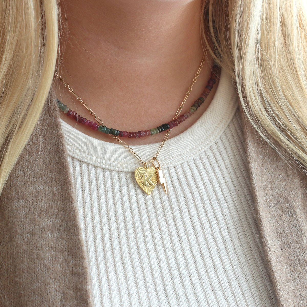 Woman in a cream sweater wearing the Watermelon Tourmaline necklace layered with a gold heart pendant