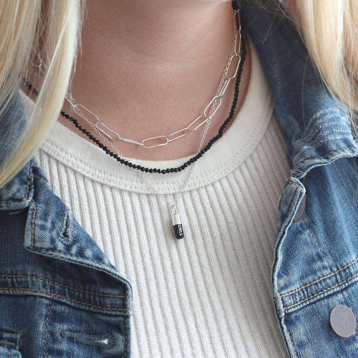 Sterling silver and black enamel Chill Pill necklace layered with chokers under a denim jacket