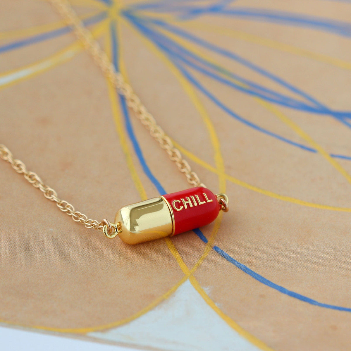 Red Big Chill Pill Chain Necklace on paper with colorful drawn lines