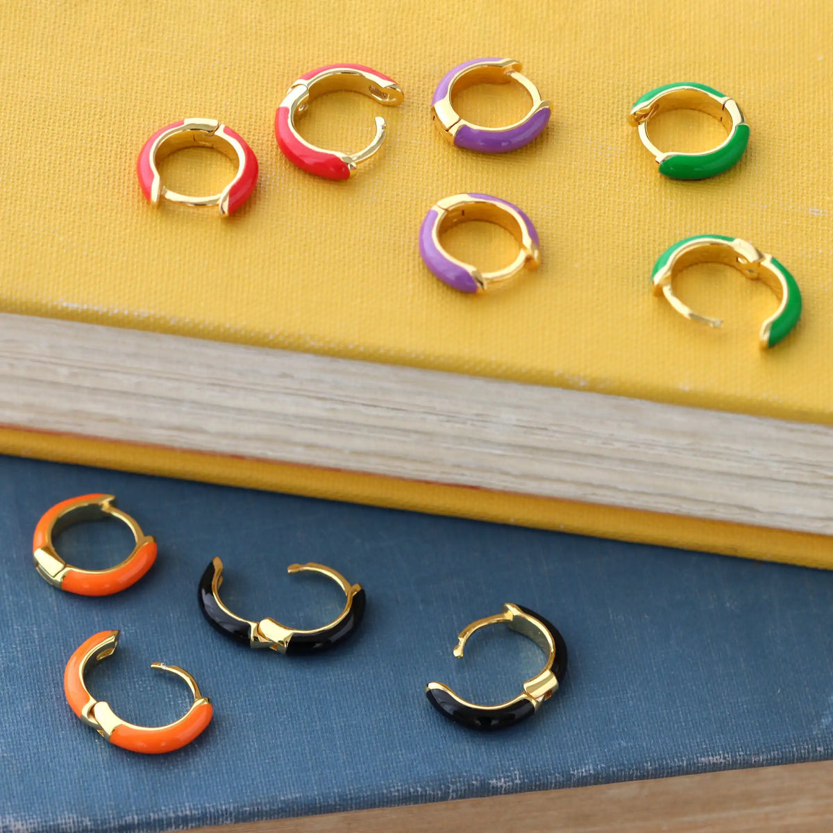 Enamel Huggie Hoop Earrings in many colors on a yellow book