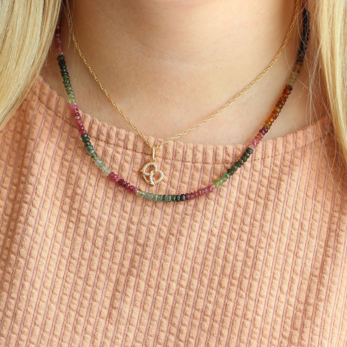 Woman in a peach sweater wearing the Watermelon Tourmaline necklace layered with a gold chain