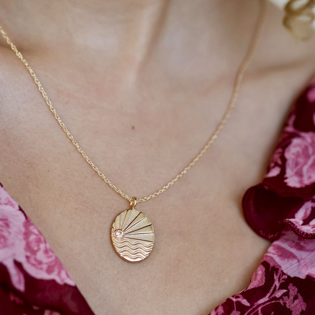 Close-up of the gold Ray of Sunshine pendant with a sun rising over waves