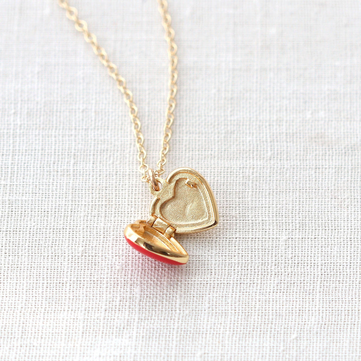 Red Enamel Heart Locket open to show the inside, on white linen