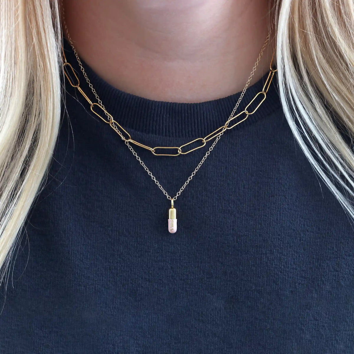Light pink Chill Pill necklace layered with a gold link chain over a black top