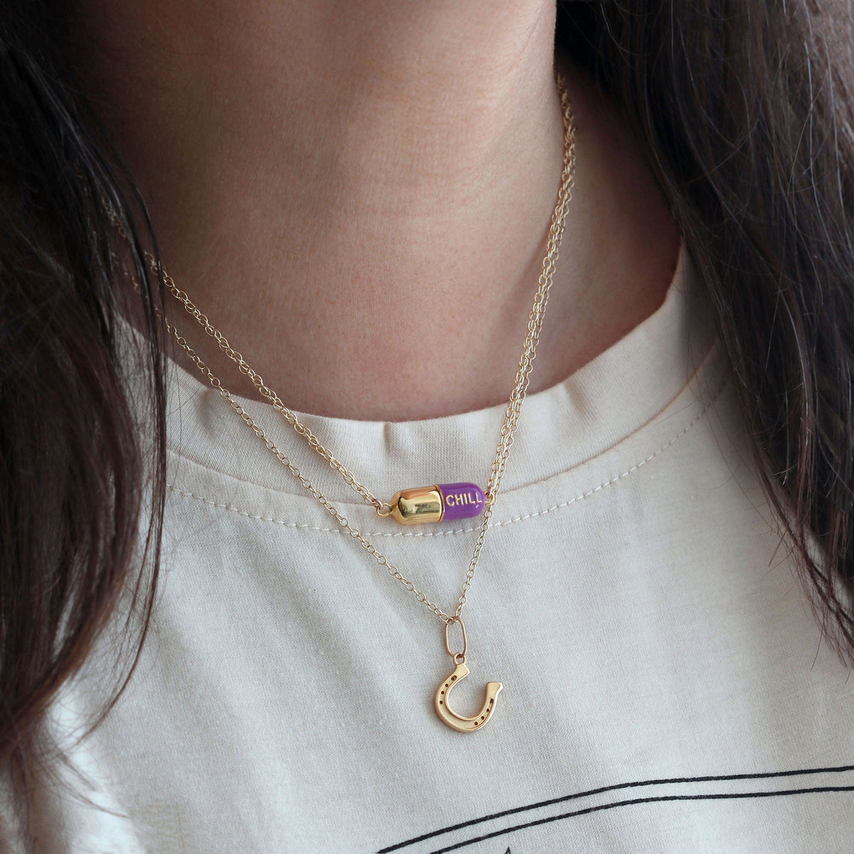 Woman in a white tee wearing the aubergine Big Chill Pill Chain Necklace layered with a horseshoe charm