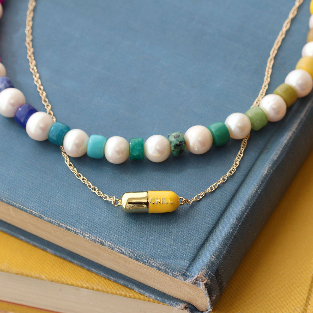 Yellow Big Chill Pill Chain Necklace with a beaded necklace on a blue book