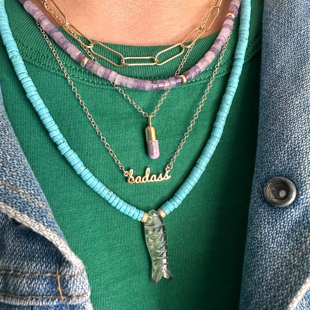 Badass Charm Necklace layered with turquoise and lavender beaded necklaces over a green top