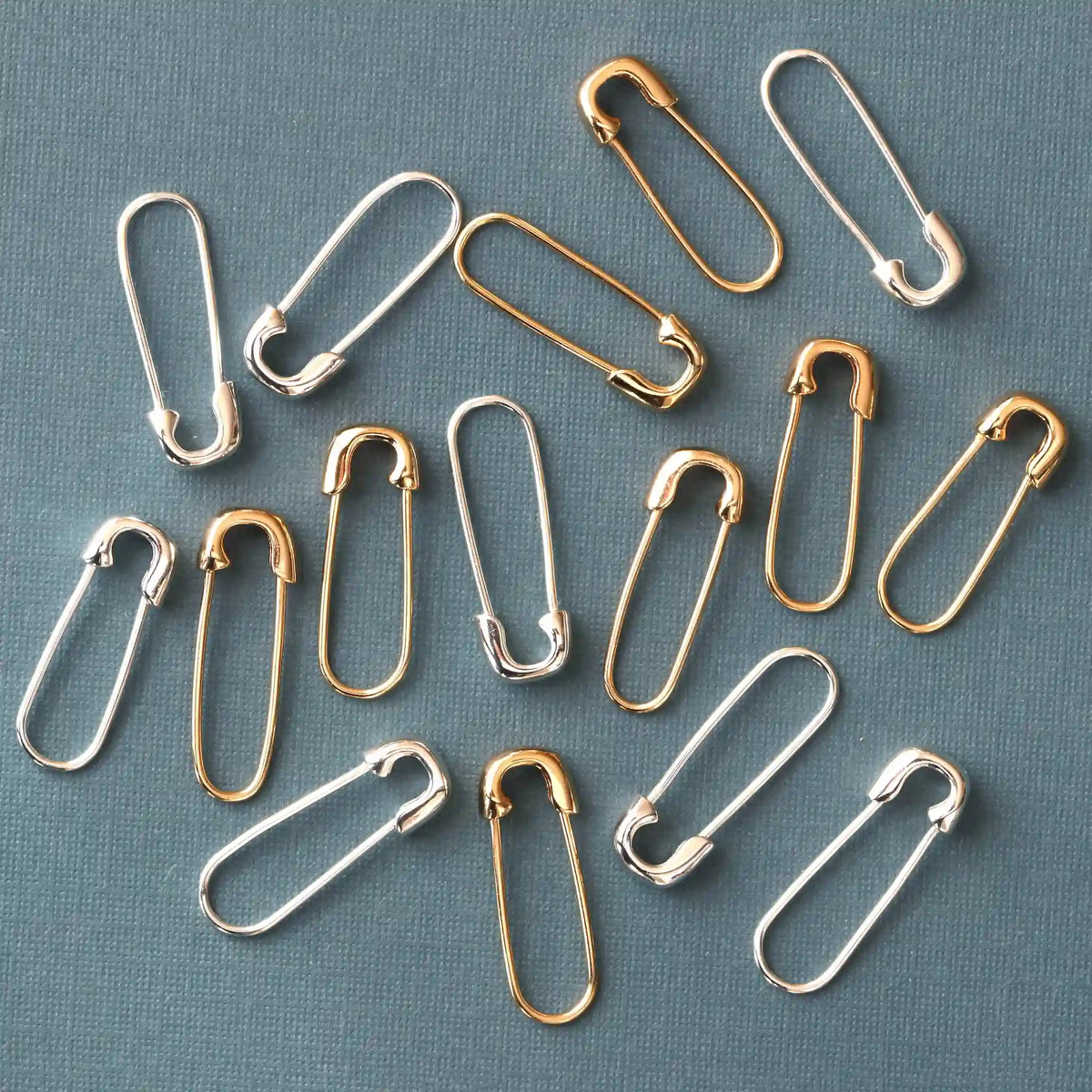 Gold and silver Classic Safety Pin Hoops scattered on a blue background