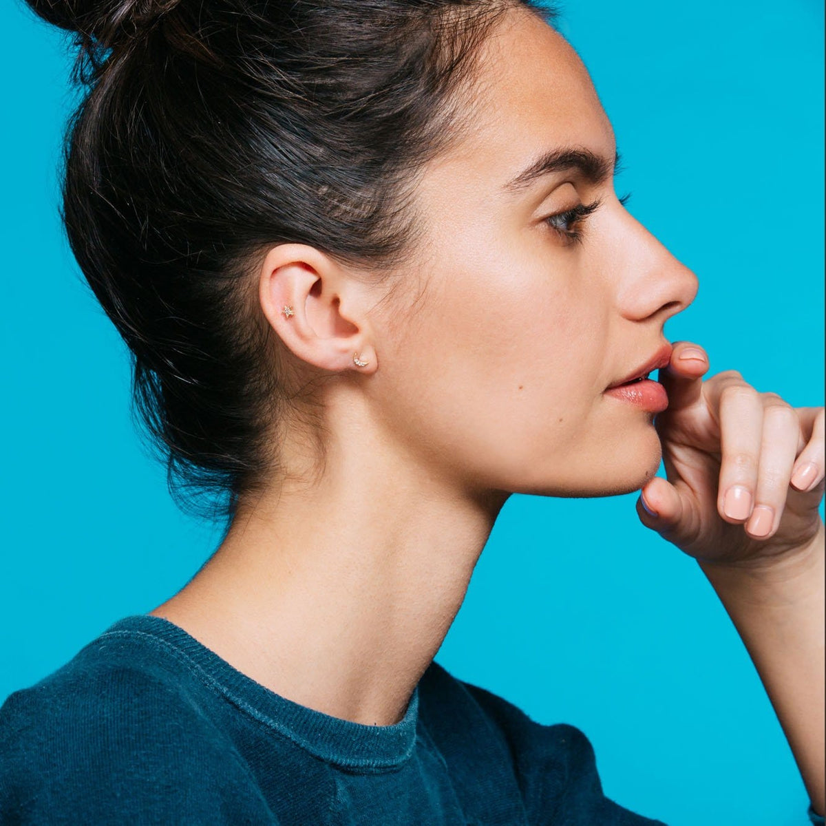 Woman with dark hair in a bun, hand at her chin, wearing gold Star and Moon Crystal Studs
