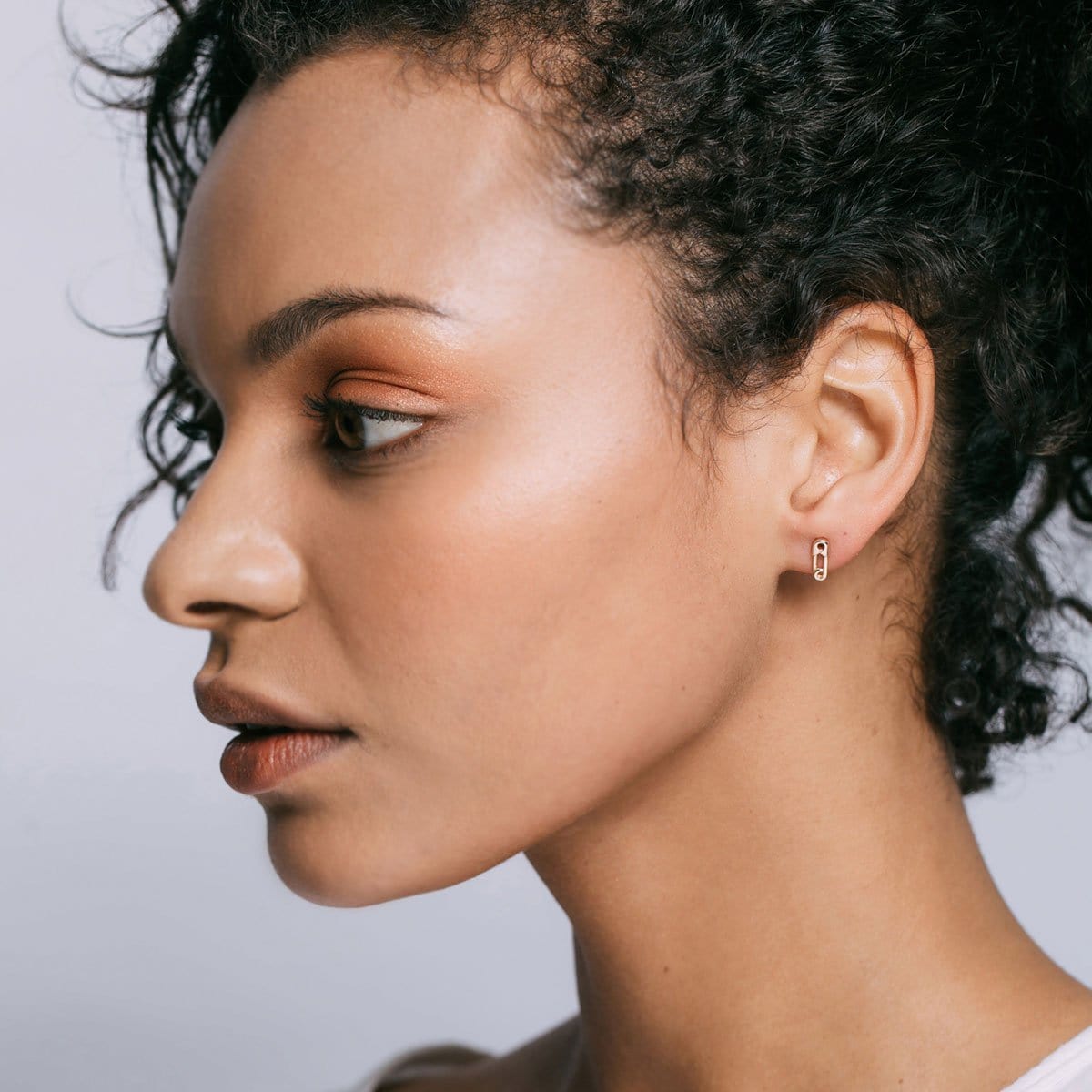 Woman with curly dark hair wearing a gold Safety Pin Stud
