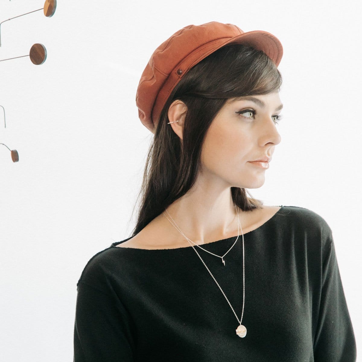 Woman in a rust beret and black top wearing the Thick As Thieves Locket layered with a second necklace