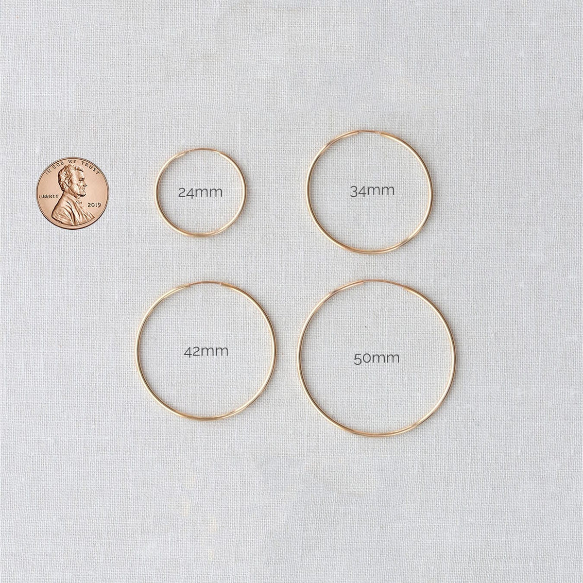 Featherweight Hoop Earrings in four sizes next to a penny for scale