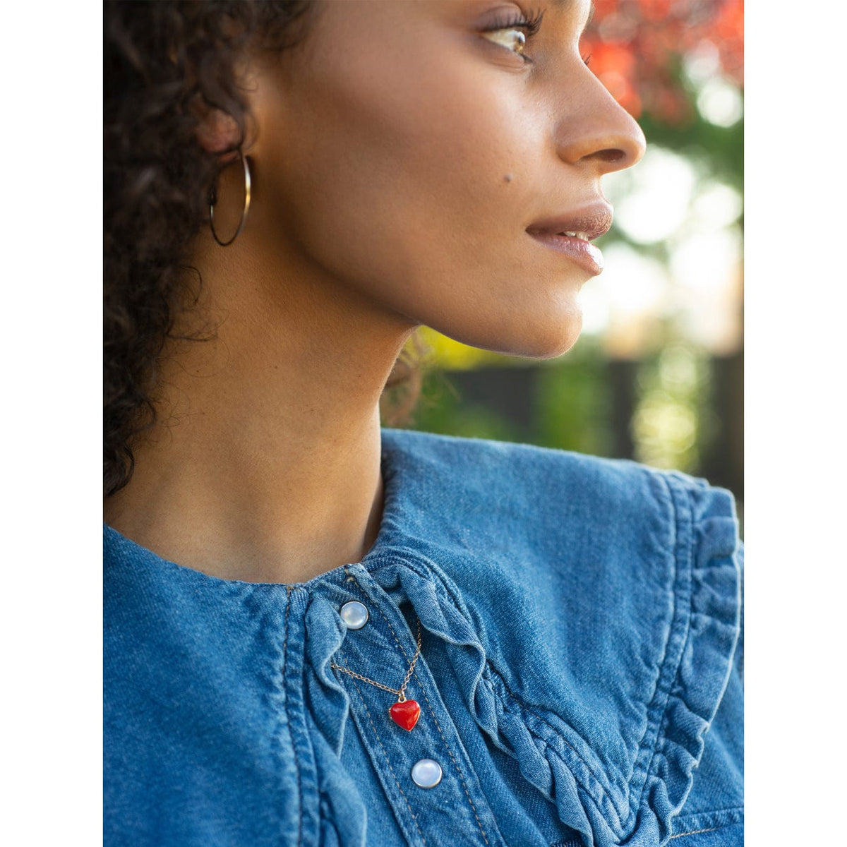 Profile of a woman with curly dark hair in a denim shirt wearing a red Enamel Heart Locket