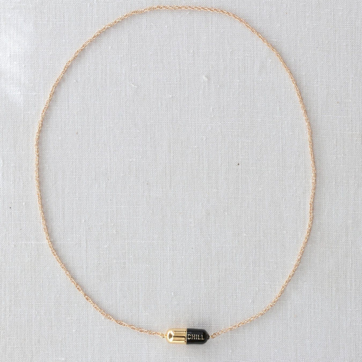 Full length of the Big Chill Pill Chain Necklace with a black pill on white linen
